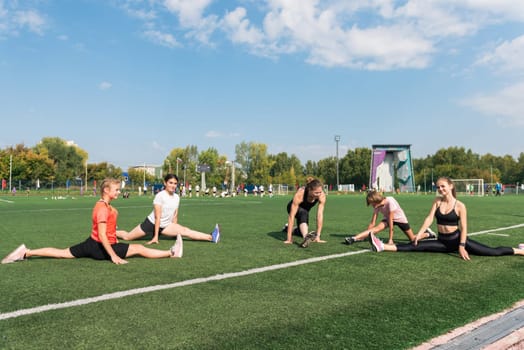 Female coach and group of children conducts a training session at the stadium outdoors