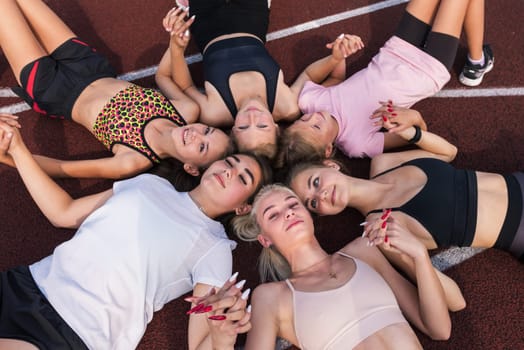 Group of tired and happy fit young girls resting on floor at stadium