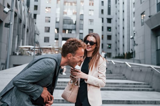 Girl holds drink. Woman and man in the town at daytime. Well dressed people.