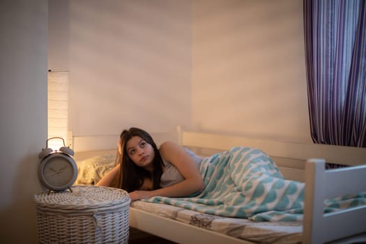 The girl lies under a blanket on the bed and rests. Bedroom in bright colors.