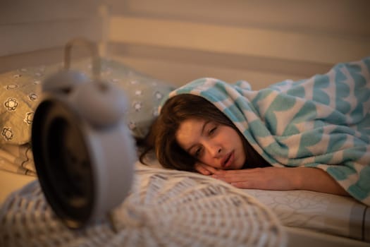 A girl under a soft blanket. The drowsy aide looks reluctantly at her alarm clock.