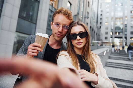 Makes selfie. Woman and man in the town at daytime. Well dressed people.