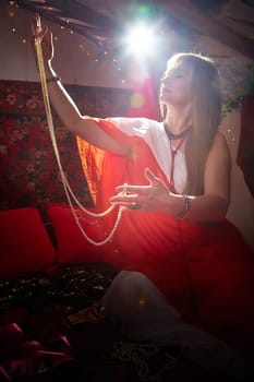 Beautiful European girl looking like Arab woman in red room with rich fabrics and carpets in sultan harem. Photo shoot of an oriental style odalisque. A model poses in sari as indian woman in india