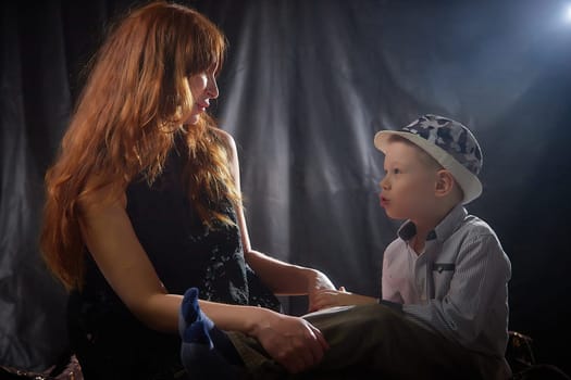 Woman with boy in hat. Mom with son on a dark background. Family portrait with mother with red hair and boy having fun together