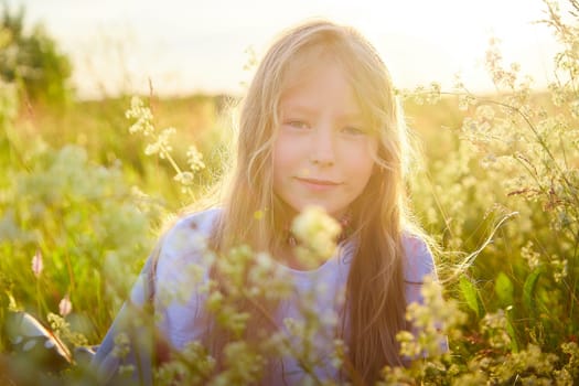 Portrait of pretty blonde girl having fun in a meadow on a natural landscape with grass and flowers on a sunny summer day. Portrait of a teenage child in summer or spring outdoors on field