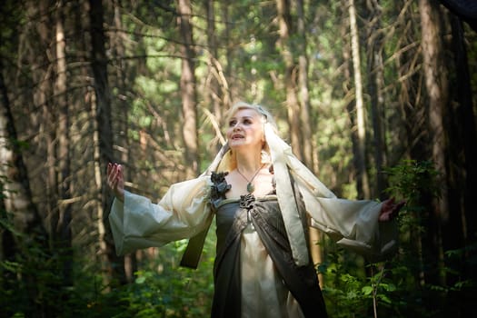 Adult mature woman 40-60 in a green long fairy dress in forest. Photo shoot in style of dryad and queen of nature. Fairy in beautiful green summer forest. Concept of caring for nature