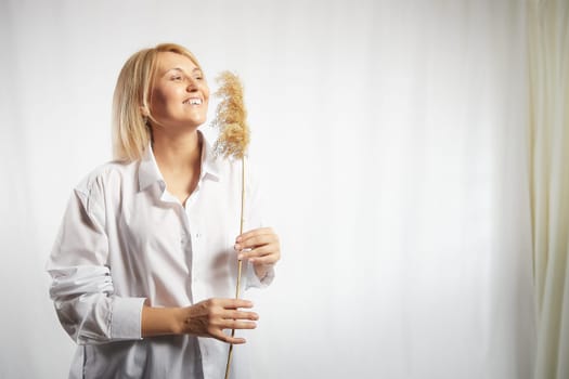 Portrait of a pretty blonde smiling woman with soft ear in hands posing on a white background. Happy girl model in white shirt in studio. The concept of softness, tenderness and dreams. Copy space