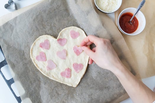Heart shaped pizza dough, chef lays heart shaped sausage. Italian pizza, heart shaped pizza