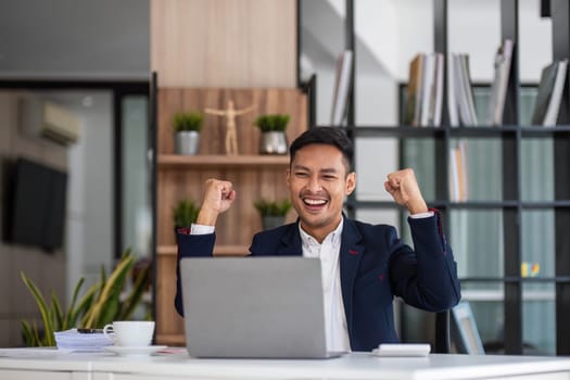 Happy young businessman looking at laptop computer in office, Excited asian man working at his workplace at modern co-working, successful people..