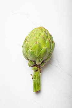 Fresh raw organic farm one artichoke on white marble background top view, healthy artichokes in balanced nutrition and cooking concept