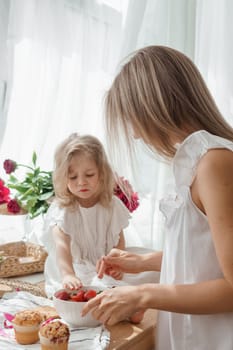 A little blonde girl with her mom on a kitchen countertop decorated with peonies. The concept of the relationship between mother and daughter. Spring atmosphere