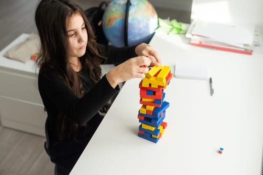 a little happy girl is playing the board game jenga at the table. Construction of a tower made of wooden cubes.