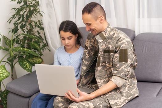 Happy military man smiling and hugging his family while using laptop indoors.