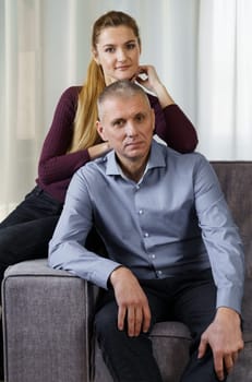 A married couple is sitting on a sofa in an apartment. Vertical frame.