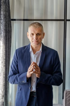 Portrait of a mature calm businessman with his jacket unbuttoned and palms folded in front.