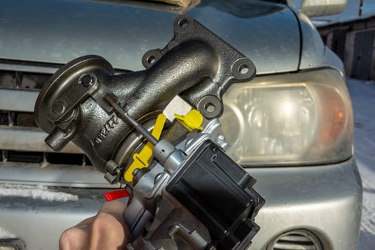 A turbine for an automobile engine in the hands of an auto mechanic on the background of a car. Maintenance and repair of the car in the car service.