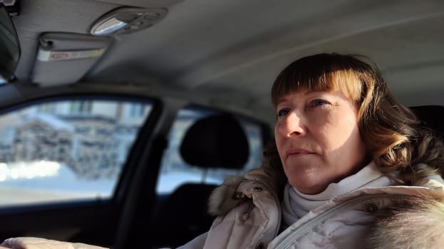 Woman sitting in the car in road trip. Blonde senior Woman driving transport. Lady travelling in cold time