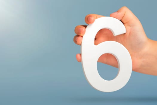 Number six in hand. A hand holds a white number 6 on a blue background with copy space. Concept with number six. 6 percent, birthday 6, sixth grade, in sixth grade.