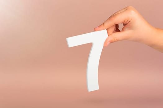 Number seven in hand. Hand holding white number 7 on red background with copy space. Concept with number seven. Birthday 7 years, percent, seventh grade or day