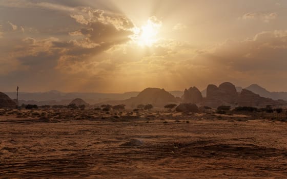 Typical landscape in Alula region near Hegra Mada in Salih archaeological site just before sunset sandy arid desert with few trees and small mountains at distance