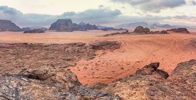 Rocky scenery in Wadi Rum desert during morning, small camp tents visible at distance.