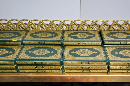 Stacks of green and golden Quran or Quraan books at shelf, closeup detail.