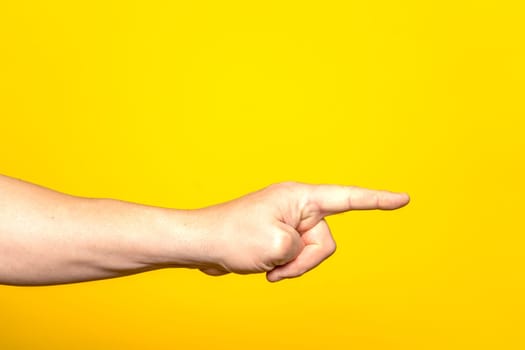 Man's hand pointing at something with the index finger, isolated on yellow background. Choice gesture. Side view.