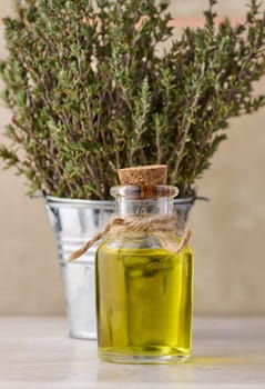 A clear glass bottle with oil and fresh thyme branches in a miniature bucket on a wooden table, cosmetic procedure oil