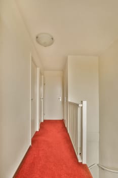 a long hallway with red carpet and white walls in an apartment building, taken from the front door to the left