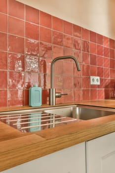 a kitchen with red tiles on the wall and wooden counter tops in front of the sink, which is being used for cleaning