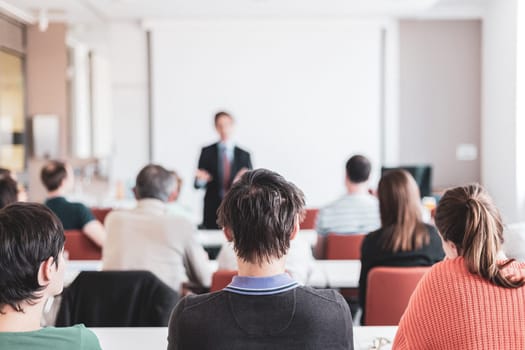 Speaker giving presentation in lecture hall at university. Participants listening to lecture and making notes. Copy space for brand on white screen.