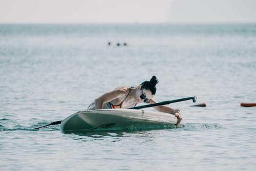 Sea woman sup. Silhouette of happy middle aged woman in rainbow bikini, surfing on SUP board, confident paddling through water surface. Idyllic sunset. Active lifestyle at sea or river