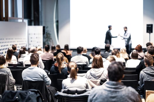 Startup team giving a pitch deck presentation in conference hall at business event. Audience at the conference hall. Business and Entrepreneurship concept. Focus on unrecognizable people in audience.