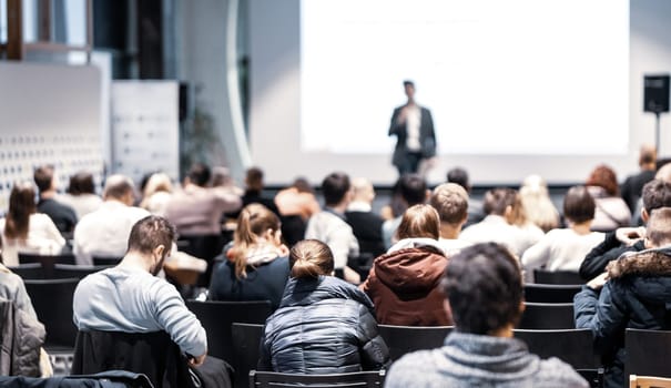 Speaker giving a talk in conference hall at business event. Rear view of unrecognizable people in audience at the conference hall. Business and entrepreneurship concept.