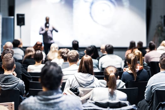 Speaker giving a talk in conference hall at business event. Rear view of unrecognizable people in audience at the conference hall. Business and entrepreneurship concept.