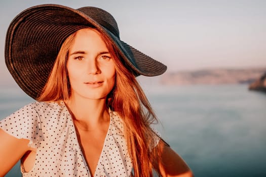 Portrait of happy young woman wearing summer black hat with large brim at beach on sunset. Closeup face of attractive girl with black straw hat. Happy young woman smiling and looking at camera at sea