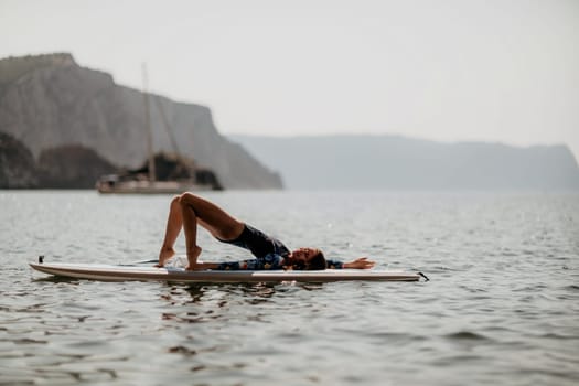 Woman sup yoga. Middle age sporty woman practising yoga pilates on paddle sup surfboard. Female stretching doing workout on sea water. Modern individual hipster outdoor summer sport activity