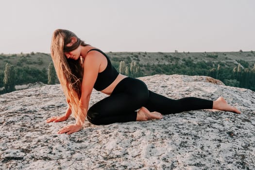 Well looking middle aged woman with long hair, fitness instructor in leggings and tops doing stretching and pilates on the rock near forest. Female fitness yoga routine concept. Healthy lifestyle.