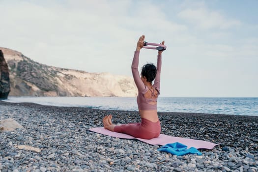 Middle aged well looking woman with black hair doing Pilates with the ring on the yoga mat near the sea on the pebble beach. Female fitness yoga concept. Healthy lifestyle, harmony and meditation.