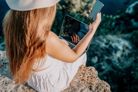 Successful business woman in yellow hat working on laptop by the sea. Pretty lady typing on computer at summer day outdoors. Freelance, travel and holidays concept.