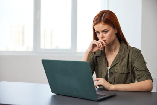 portrait of a red-haired woman in the office sitting thoughtfully at a laptop. High quality photo