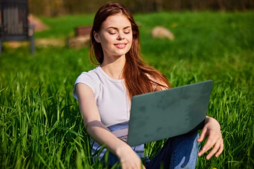 portrait of a woman sitting at a laptop in a field with a laptop in her hands. High quality photo
