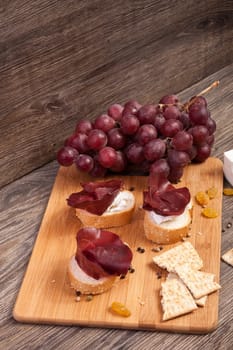 Mixed antipasto from grape, crackers and ham. Healthy food on wooden background