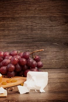 White cheese, nuts and red grape on wooden background in vintage toning. Healthy style of life