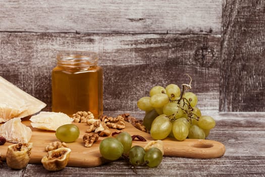Parmesan, honey, nuts and grape on wooden background in studio photo. Healthy lifestyle