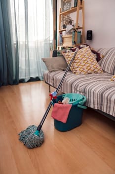 mop and bucket with cleaning products and a rag next to the sofa, home cleaning concept, no people