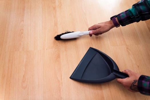 hands of a person sweeping the floor with a brush and dustpan, home cleaning concept, copy space for text