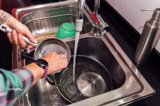 closeup of the hands of a person cleaning the dishes and pans on a sink, concept of cleaning at home and in the kitchen