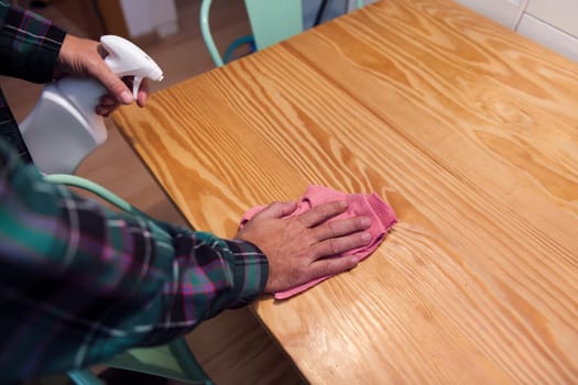 closeup of the hands of a person cleaning a wooden table with a rag and a spray, home cleaning concept, copy space for text