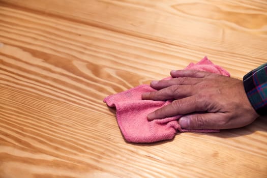 closeup of the hand of a person cleaning a wooden table with a rag, home cleaning concept, copy space for text